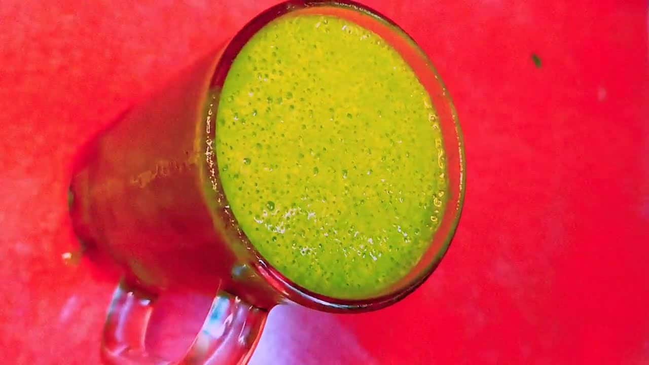 A glass mug filled with a green smoothie sits on a bright red surface.